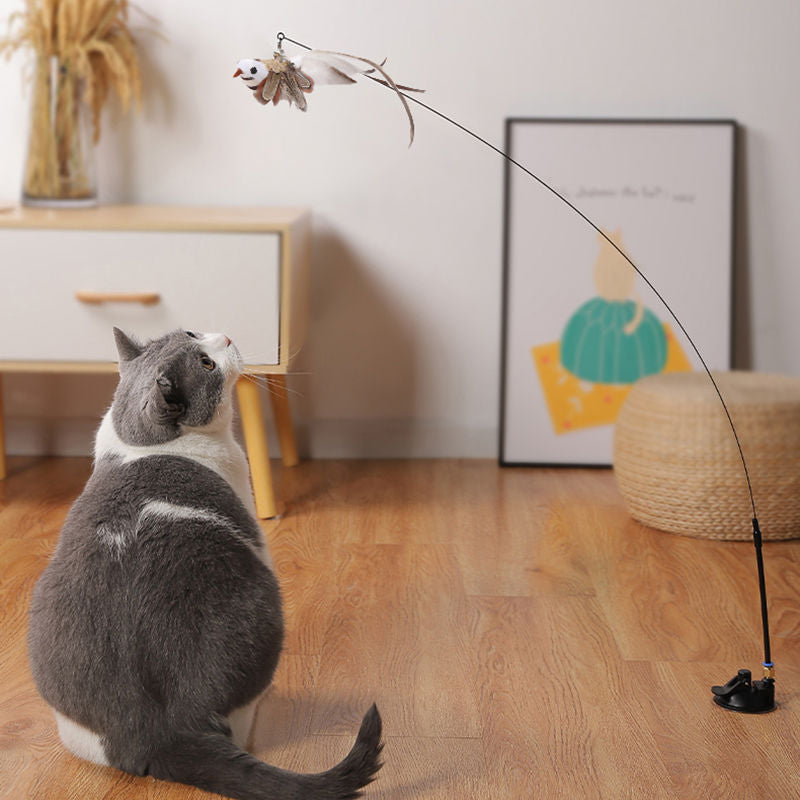 Grey and white cat looking up at an Aevvon feather wand cat toy on a bent rod indoors